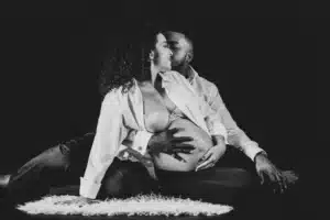 Couple enceinte en noir et blanc, l'homme embrasse sa femme. Leurs mains caressent le ventre rond, moment tendre de maternité.